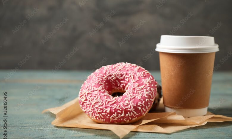 Yummy donuts with sprinkles and paper cup on wooden table