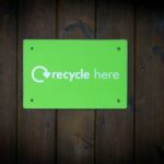a green recycle here sign on a wooden wall